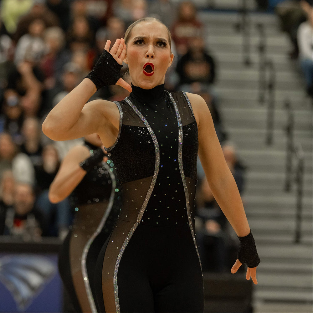 Dancer in a black and silver outfit performing on stage with a blurred audience in the background